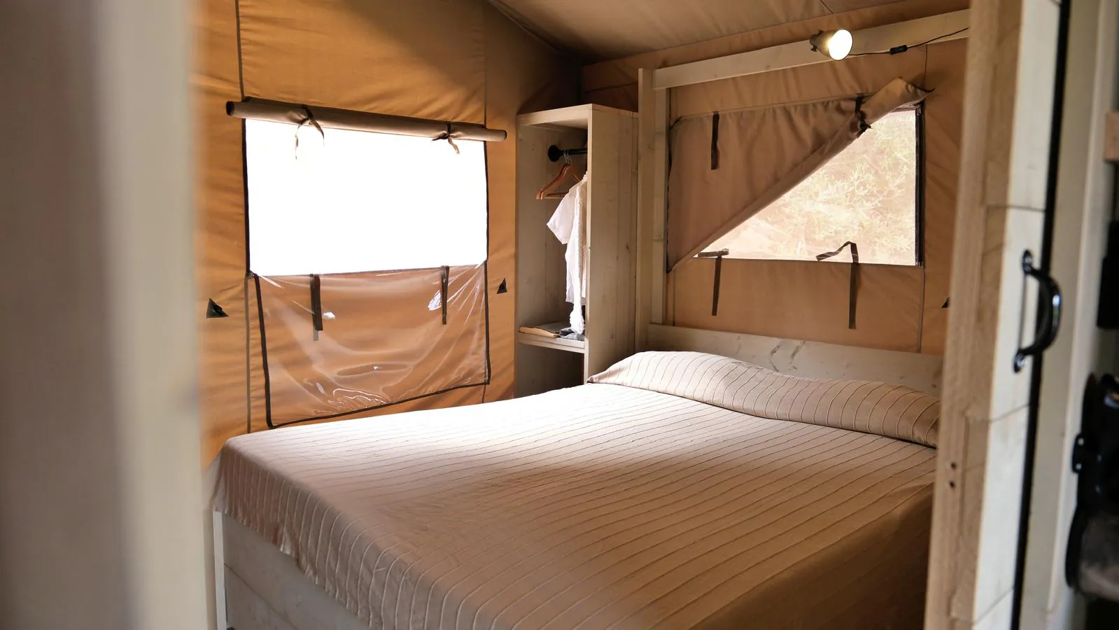 La camera matrimoniale del lodge vista dalla porta, con letto, pareti in tela e finestre sulla vegetazione