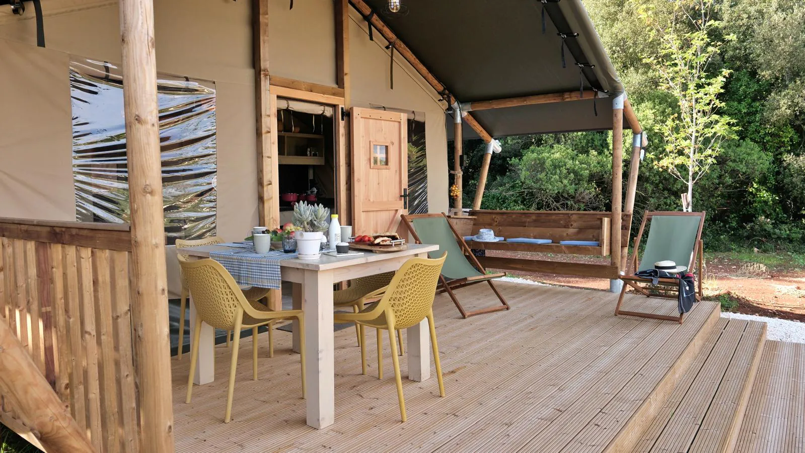 La veranda con tavolo, sedute e dondolo, davanti all’ingresso aperto del glamping